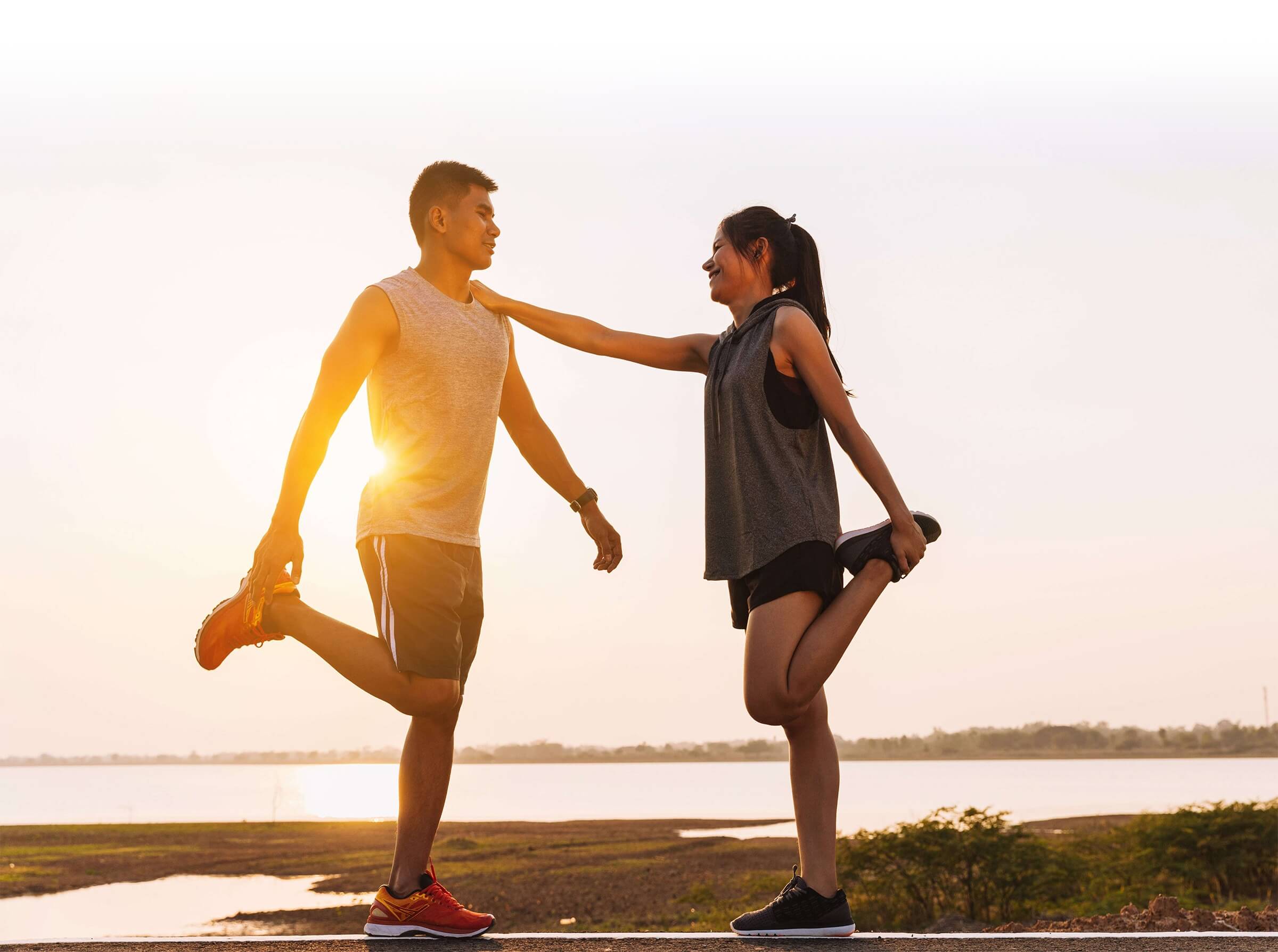Man and woman stretching together outdoors at sunset, promoting fitness, wellness, and healthy lifestyle