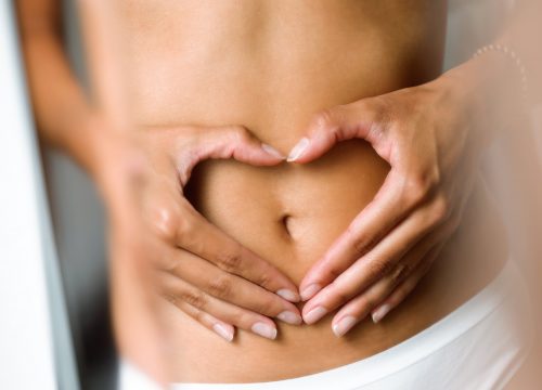 Photo of a woman's hands making a heart shape over her flat stomach