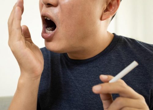 Photo of a yawning man holding a cigarette