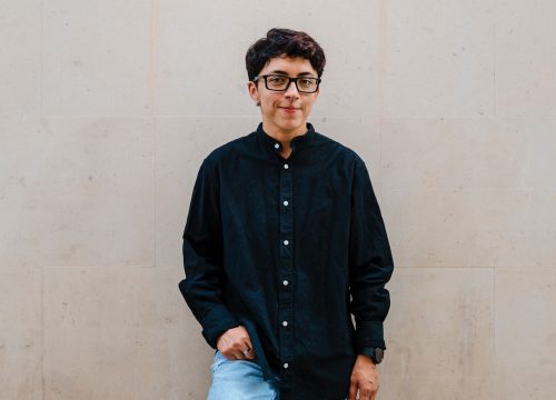 Photo of a trans man wearing glasses, a black shirt, and jeans